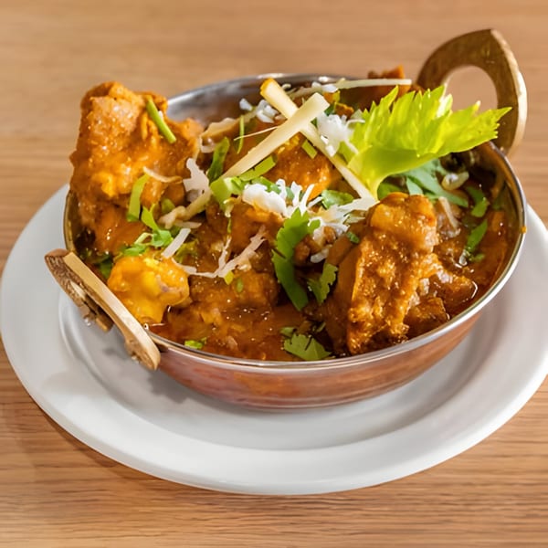 Himalayan Spice & Savor's Indian chicken curry in a copper bowl, garnished with cilantro and ginger.