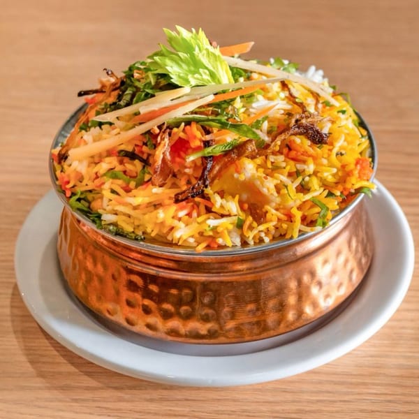 Indian chicken biryani, a flavorful rice dish with chicken, vegetables, and spices, served in a copper bowl.