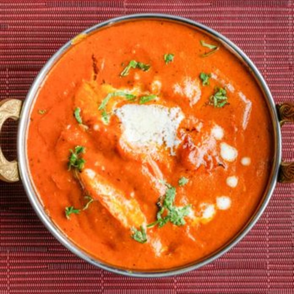 A metal bowl of vibrant orange Indian curry, garnished with cream and fresh cilantro.