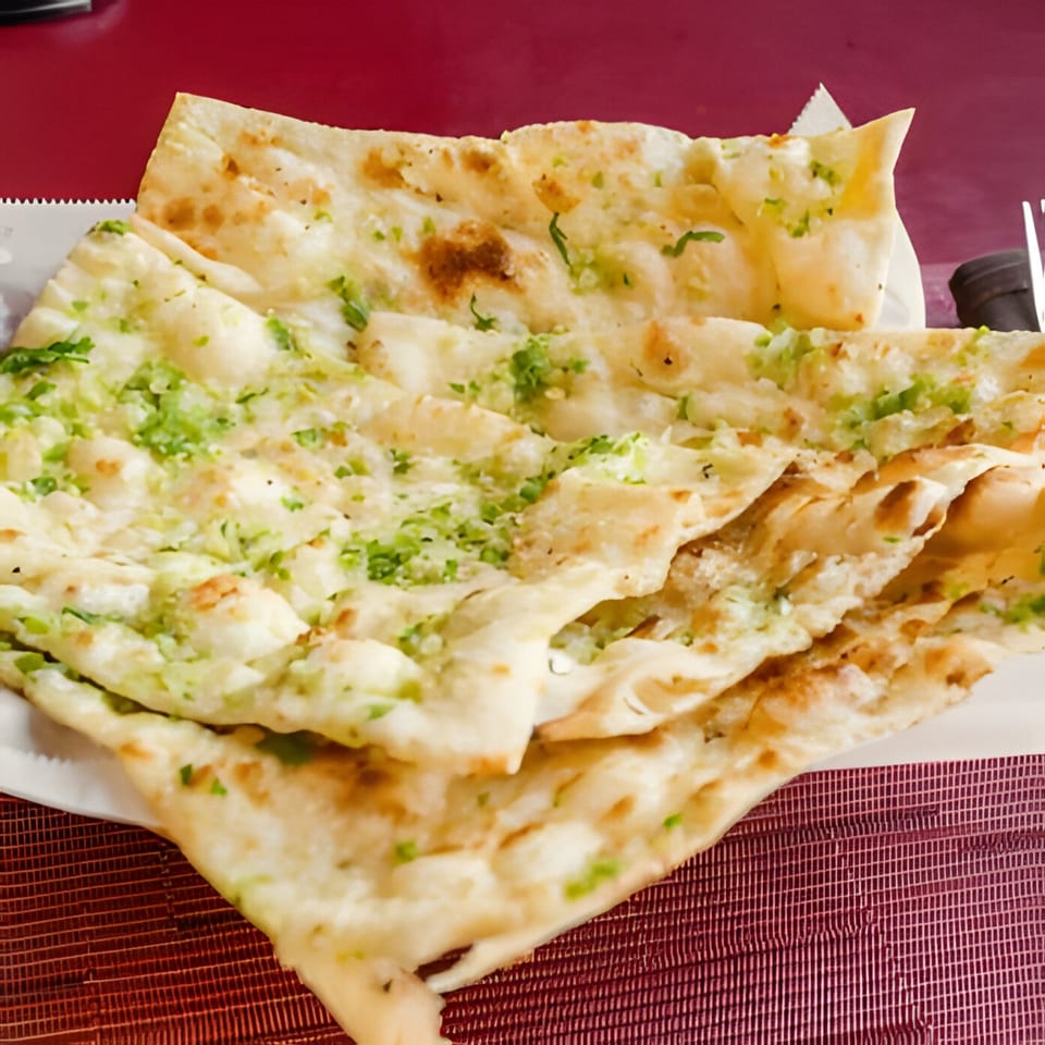 Garlic naan bread, topped with green herbs, served on a white plate at HIMALAYAN SPICE & SAVOR.