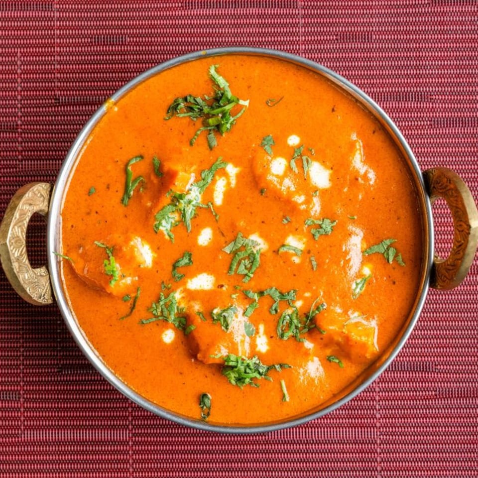 HIMALAYAN SPICE & SAVOR's Indian butter chicken, garnished with cilantro, in a metal serving bowl.