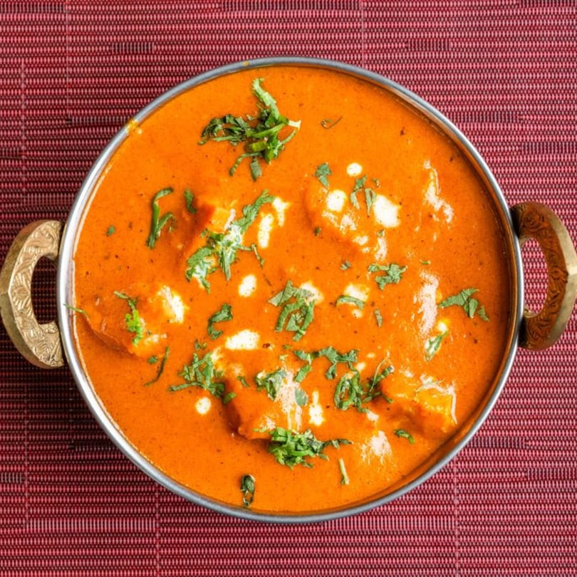HIMALAYAN SPICE & SAVOR's Indian butter chicken, garnished with cilantro, in a metal serving bowl.