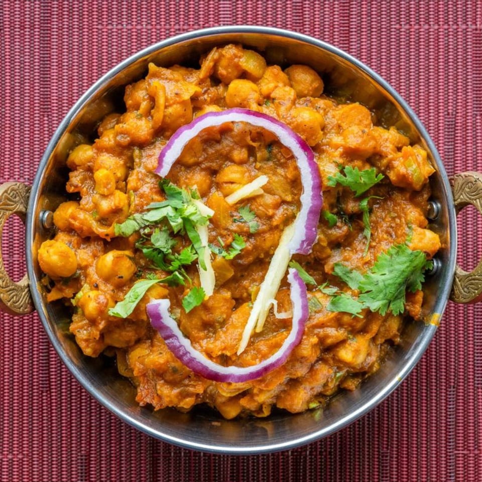 HIMALAYAN SPICE & SAVOR's Chana Masala, a chickpea curry, garnished with red onion and cilantro.