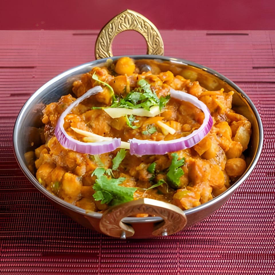 Indian chana masala in a metal bowl, garnished with red onion, ginger, and cilantro.