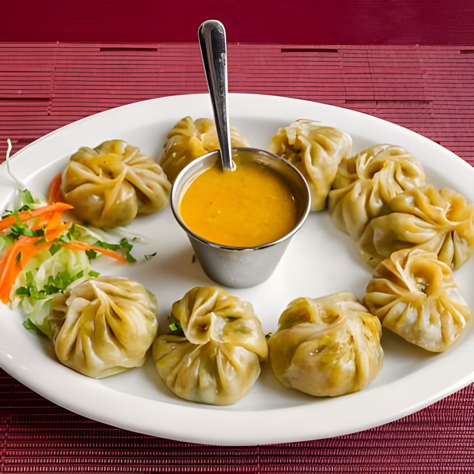 A plate of Himalayan momos, with a side of salad and a small bowl of orange dipping sauce.